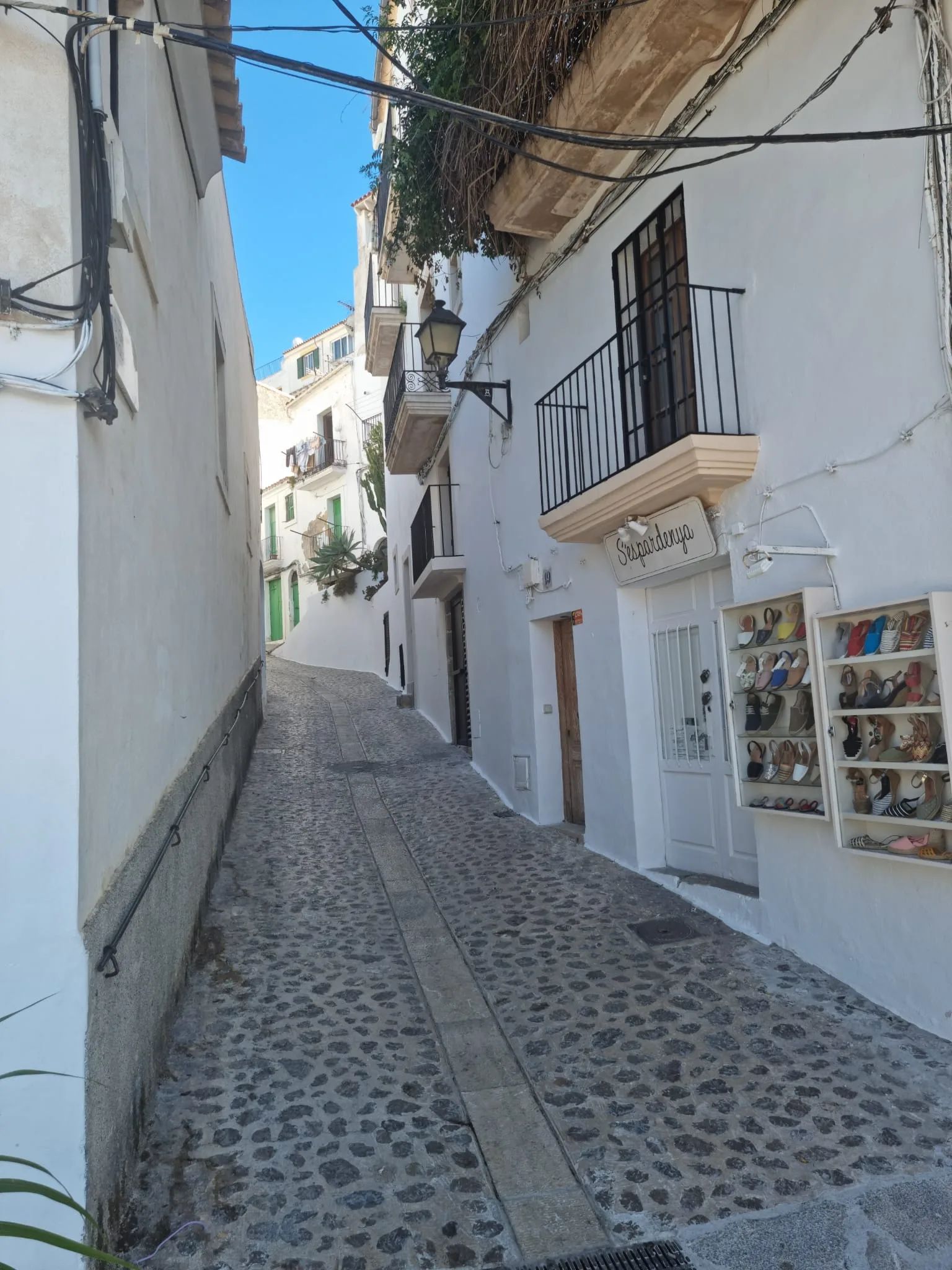 Calle estrecha y empedrada con una tienda tradicional de espardenyas (alpargatas) en Dalt Vila