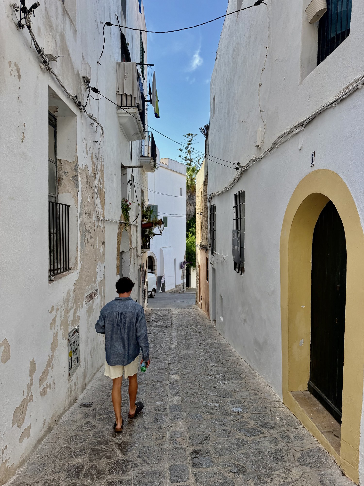 Calle empedrada y encalada con un arco amarillo característico en el casco antiguo de Dalt Vila, Ibiza.